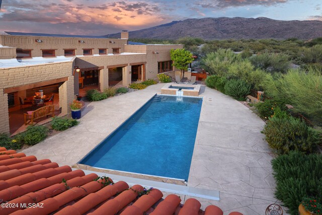 pool at dusk featuring a patio, an in ground hot tub, a mountain view, and an outdoor pool