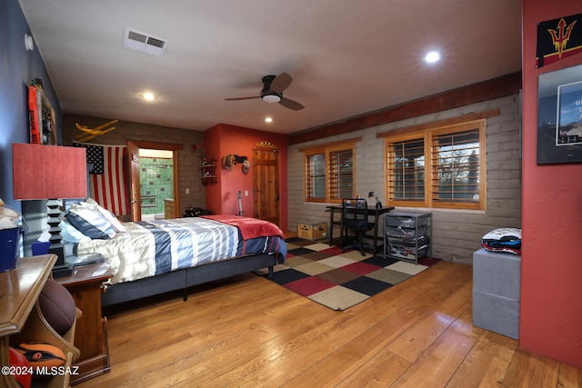 bedroom with a ceiling fan, hardwood / wood-style flooring, brick wall, and visible vents