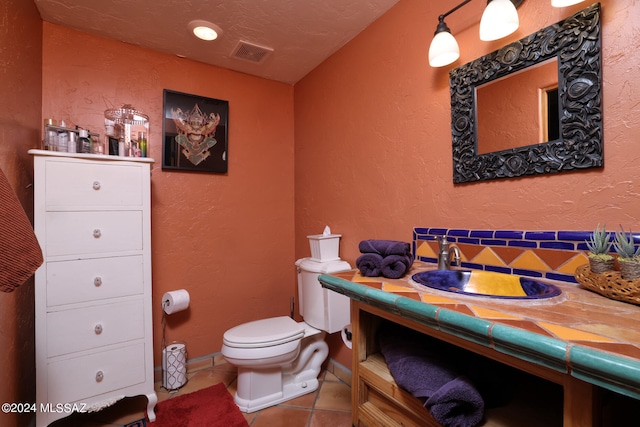 bathroom with tile patterned flooring, visible vents, a textured wall, vanity, and toilet