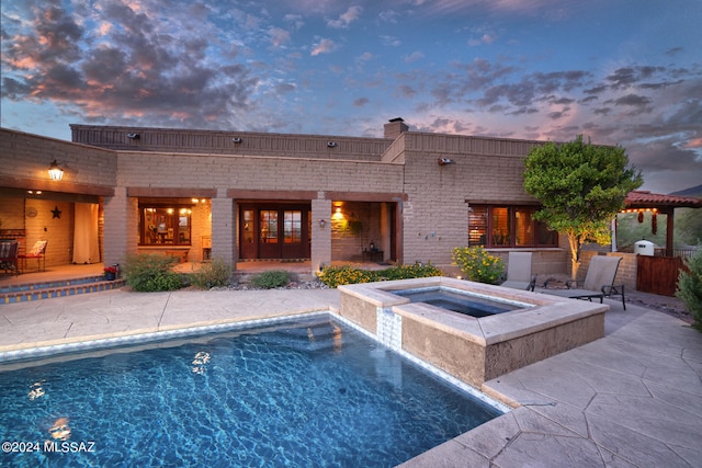 back of property with brick siding, an in ground hot tub, an outdoor pool, and a patio area