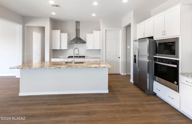 kitchen with a center island with sink, wall chimney range hood, stainless steel appliances, and white cabinets