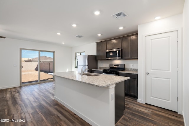 kitchen with light stone counters, appliances with stainless steel finishes, a kitchen island with sink, dark wood-type flooring, and sink