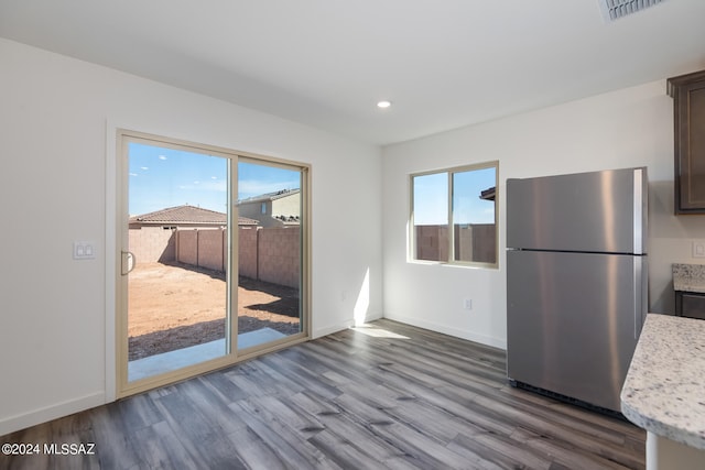 kitchen featuring light stone countertops, dark brown cabinets, hardwood / wood-style flooring, and stainless steel fridge