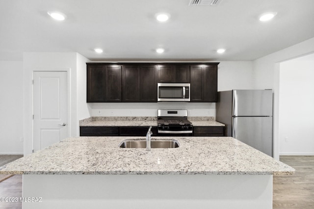 kitchen with stainless steel appliances, a center island with sink, sink, and light hardwood / wood-style floors