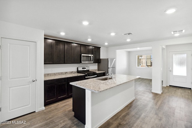 kitchen with a center island with sink, stainless steel appliances, hardwood / wood-style flooring, light stone counters, and sink