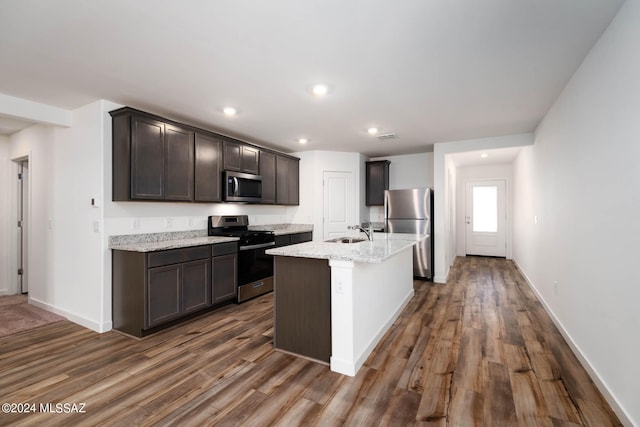 kitchen with light stone countertops, stainless steel appliances, an island with sink, dark hardwood / wood-style floors, and sink