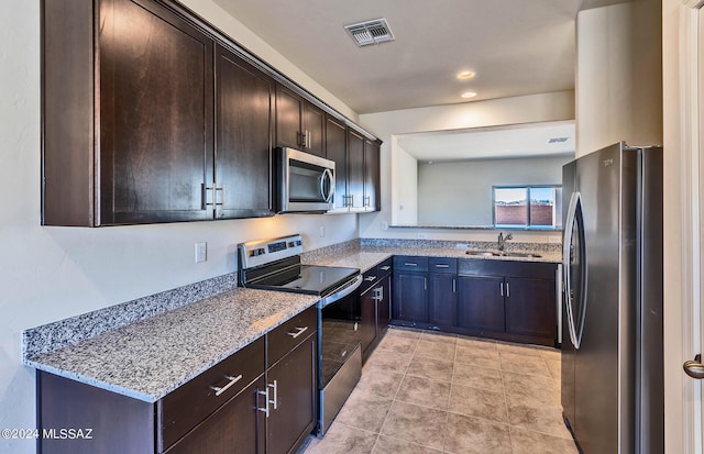 kitchen featuring appliances with stainless steel finishes, dark brown cabinetry, light stone counters, and sink