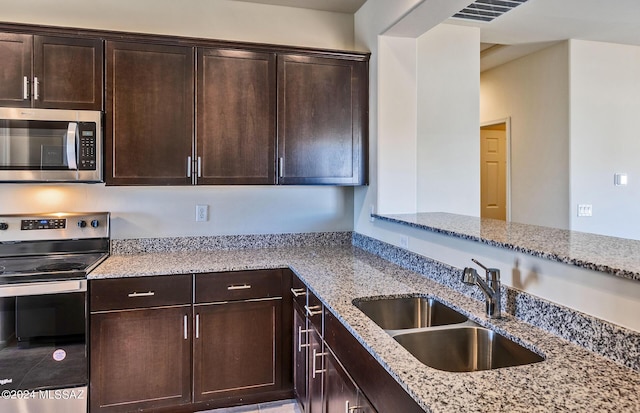 kitchen featuring dark brown cabinetry, stainless steel appliances, light stone counters, and sink