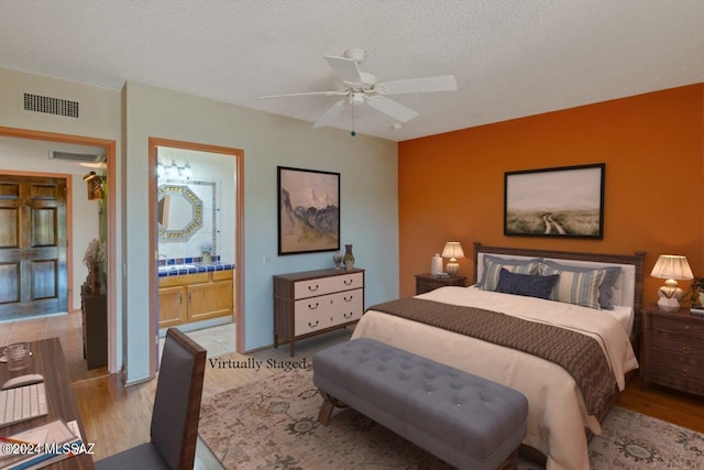 bedroom with visible vents, ensuite bath, light wood-style flooring, and a textured ceiling