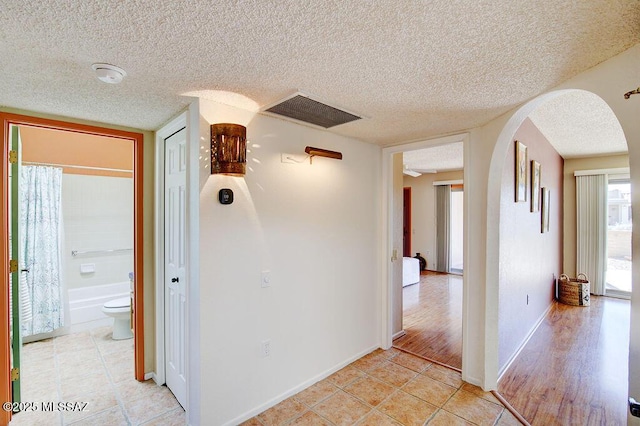 corridor with arched walkways, light tile patterned floors, visible vents, a textured ceiling, and baseboards