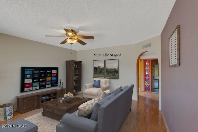 living room featuring arched walkways, visible vents, a ceiling fan, a textured ceiling, and light wood-type flooring