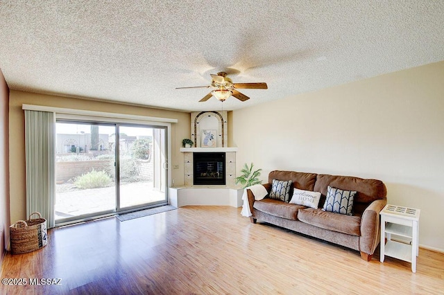 living room featuring ceiling fan, wood finished floors, a textured ceiling, and a glass covered fireplace