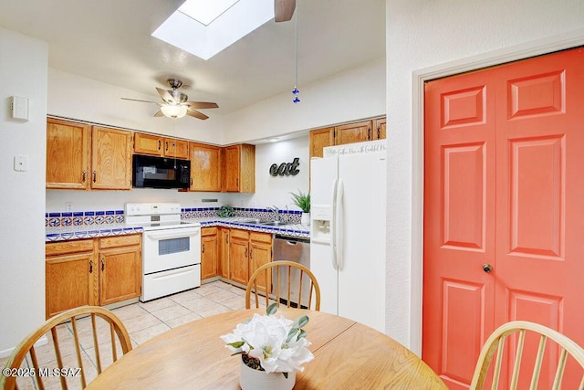 kitchen featuring a skylight, brown cabinets, light tile patterned floors, a ceiling fan, and white appliances