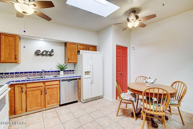 kitchen featuring white appliances, a skylight, a ceiling fan, brown cabinets, and a sink