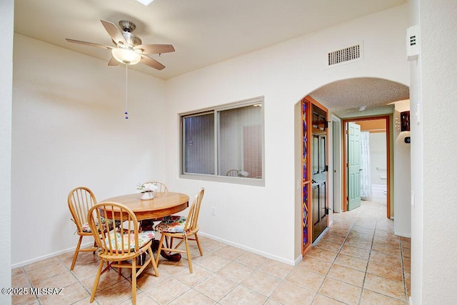 dining space featuring arched walkways, light tile patterned floors, visible vents, baseboards, and a ceiling fan