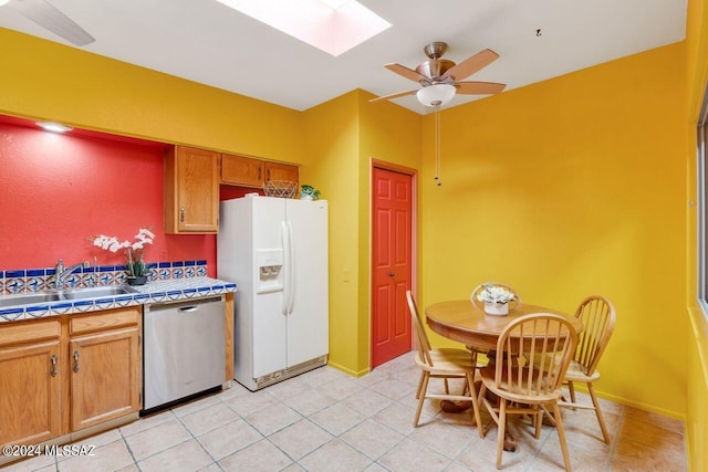 kitchen featuring tile countertops, sink, a skylight, stainless steel dishwasher, and white fridge with ice dispenser