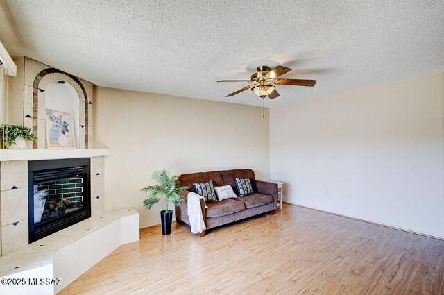 living room with a textured ceiling, a large fireplace, light hardwood / wood-style floors, and ceiling fan