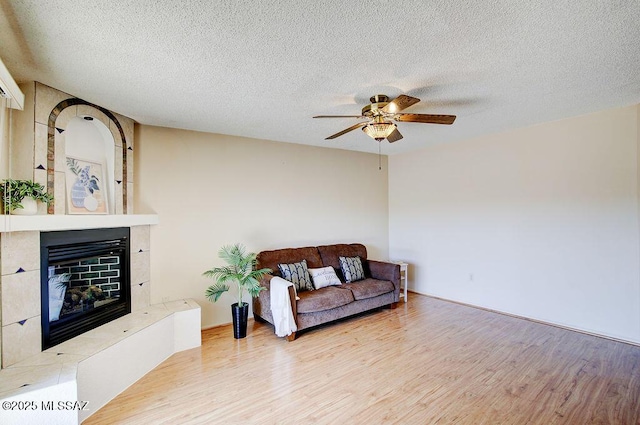 living room featuring ceiling fan, a textured ceiling, light wood-type flooring, and a glass covered fireplace