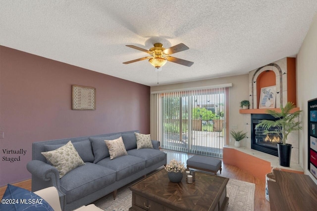 living room featuring wood-type flooring, a textured ceiling, a large fireplace, and ceiling fan