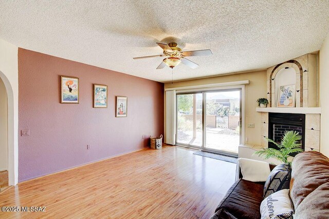 living room with light wood finished floors, a large fireplace, arched walkways, a ceiling fan, and a textured ceiling