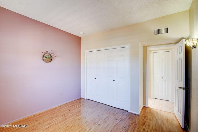 unfurnished bedroom featuring a textured ceiling, visible vents, baseboards, light wood-style floors, and a closet