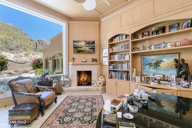 living area featuring built in shelves, ceiling fan, light tile patterned floors, a mountain view, and a tiled fireplace