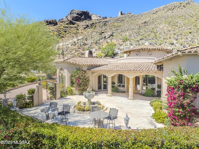 back of property with a mountain view and a patio