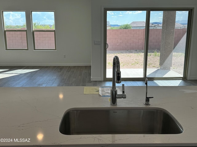 kitchen with light stone counters, wood finished floors, baseboards, and a sink