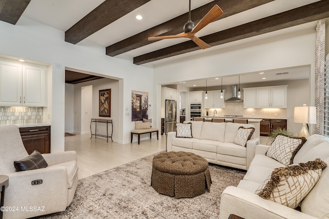 living room featuring beamed ceiling, ceiling fan, light wood-type flooring, and sink