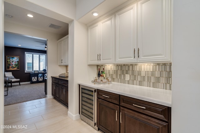 bar with white cabinetry, ceiling fan, beverage cooler, decorative backsplash, and dark brown cabinets