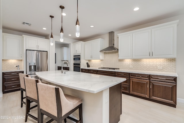 kitchen featuring stainless steel appliances, white cabinetry, wall chimney exhaust hood, and an island with sink