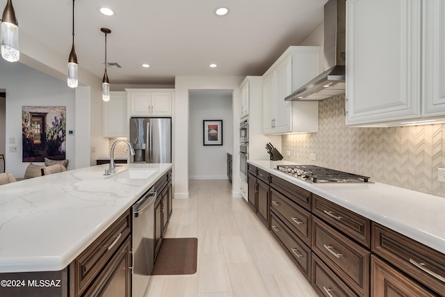 kitchen with wall chimney exhaust hood, stainless steel appliances, sink, white cabinetry, and hanging light fixtures