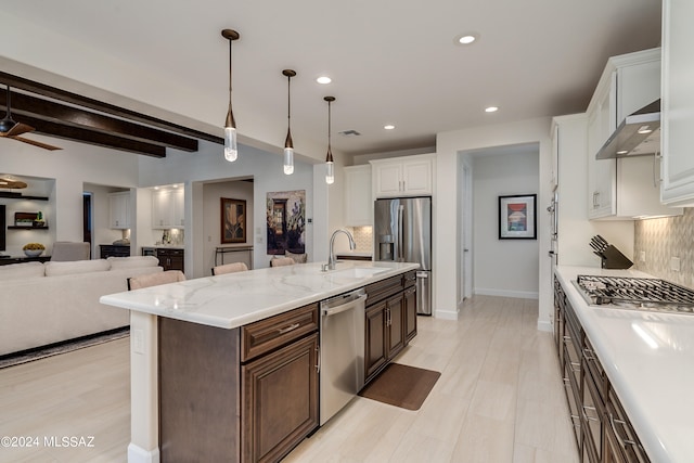 kitchen with wall chimney exhaust hood, appliances with stainless steel finishes, beamed ceiling, white cabinetry, and dark brown cabinetry