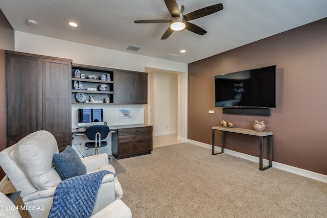 carpeted living room with ceiling fan and built in desk