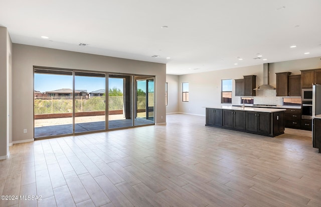 kitchen with an island with sink, wall chimney exhaust hood, and light hardwood / wood-style floors