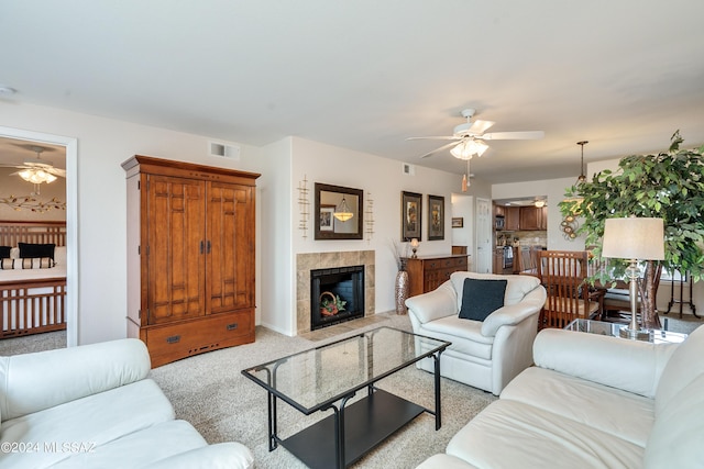 living room featuring ceiling fan, a fireplace, visible vents, and light colored carpet