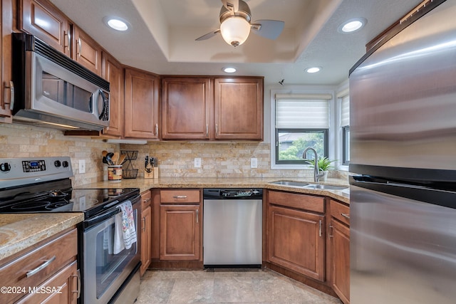 kitchen with appliances with stainless steel finishes, a raised ceiling, brown cabinets, and a sink