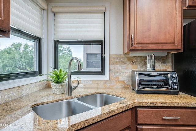 kitchen with tasteful backsplash, a toaster, brown cabinets, light stone countertops, and a sink