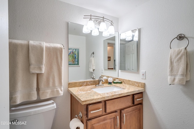 half bath featuring a textured wall, vanity, toilet, and an inviting chandelier