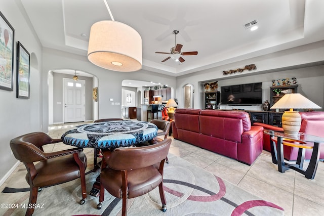 tiled dining space with ceiling fan and a raised ceiling