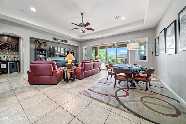 interior space with ceiling fan, beverage cooler, a tray ceiling, bar, and light tile patterned floors