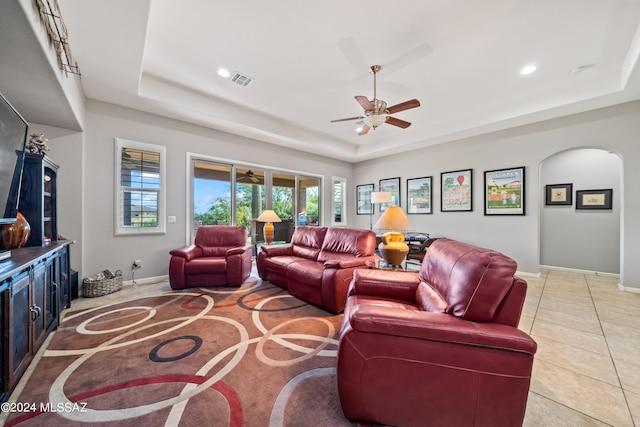 living room with ceiling fan, a raised ceiling, and light tile patterned floors