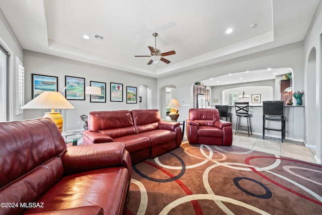 tiled living room with a tray ceiling and ceiling fan