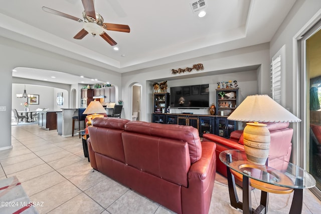 living room with light tile patterned floors, ceiling fan with notable chandelier, and a raised ceiling