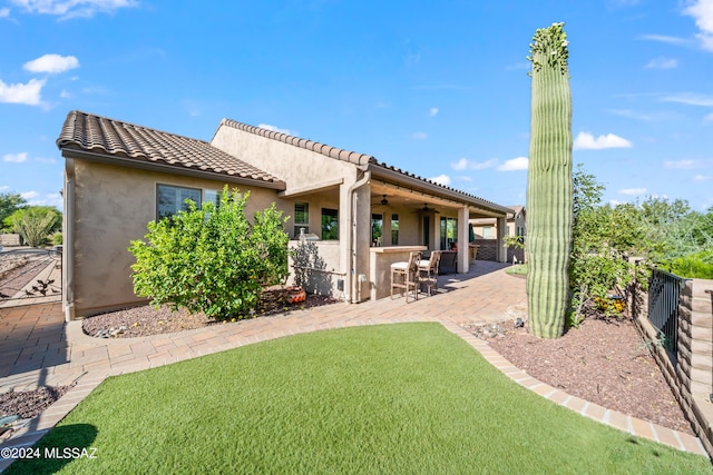 rear view of house featuring ceiling fan, a yard, exterior bar, and a patio