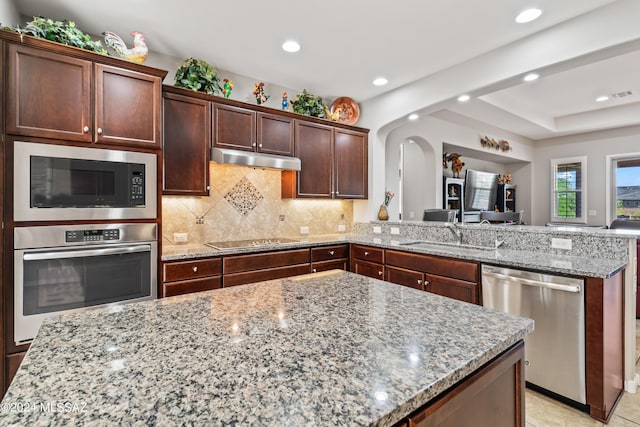 kitchen featuring light stone countertops, decorative backsplash, kitchen peninsula, stainless steel appliances, and sink