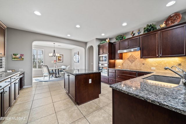 kitchen with built in microwave, sink, stainless steel oven, dark stone counters, and a kitchen island