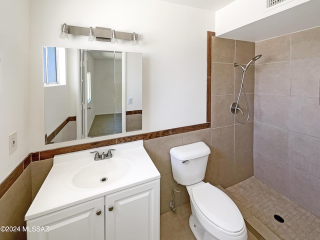 bathroom with tiled shower, vanity, tile walls, and toilet