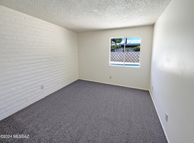 carpeted empty room featuring a textured ceiling and brick wall