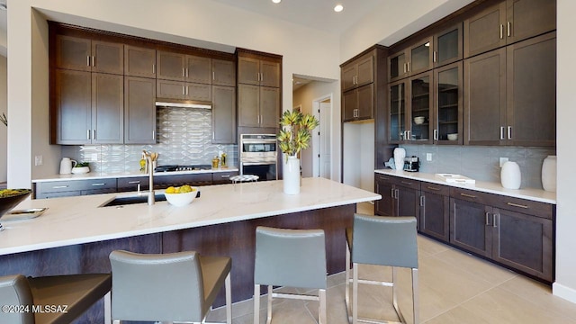 kitchen with sink, a kitchen breakfast bar, backsplash, light tile patterned floors, and appliances with stainless steel finishes